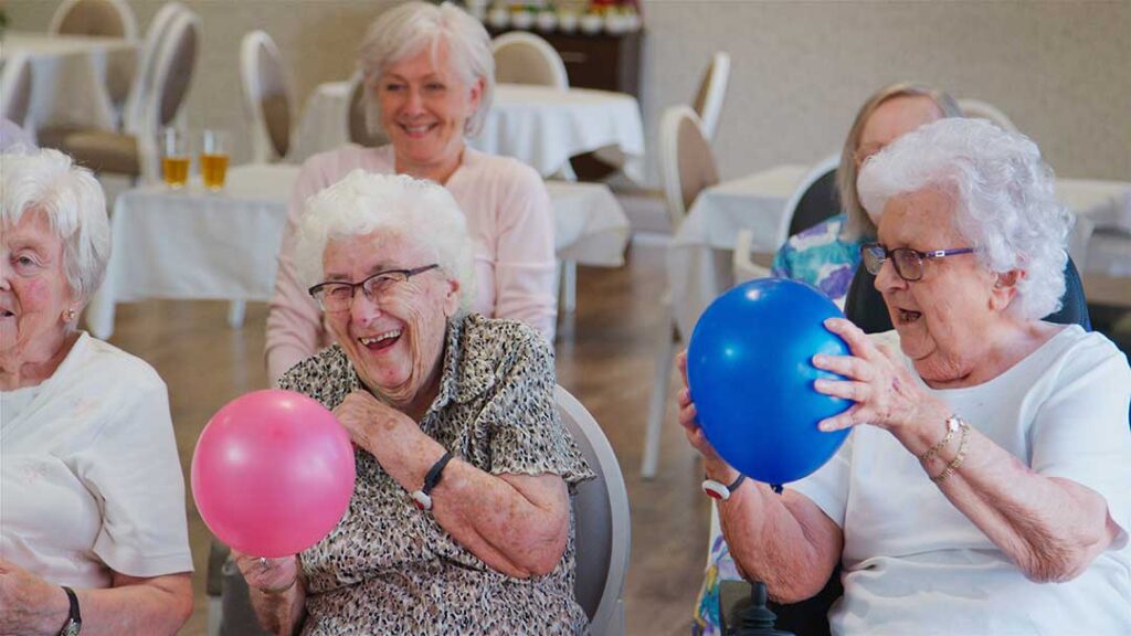 Older adults share a meal and conversation at a bright communal dining table.