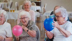 Older adults share a meal and conversation at a bright communal dining table.